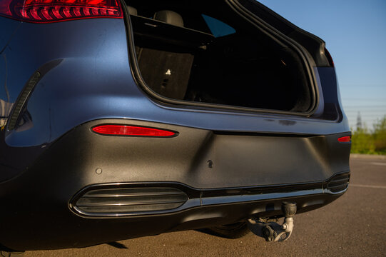 Rear bumper of a modern luxury electric car featuring parking sensors, a tow hitch, and an open trunk, close up.