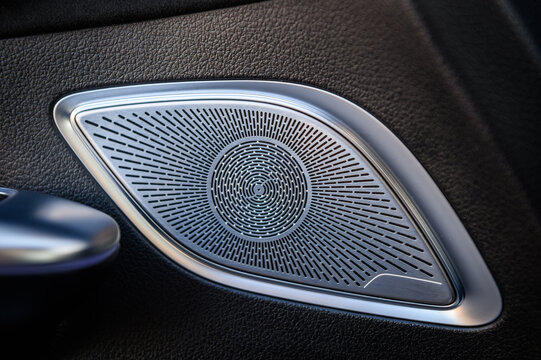 Metal speaker grille with a circular pattern integrated into the luxury car door panel, close up.