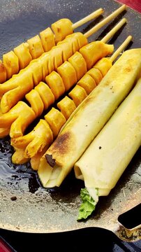 Spiral sausages and filled rolls cook together on a hot street food griddle.