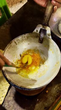 Street cook stirs a golden egg omelet in a hot pan above glowing charcoal.