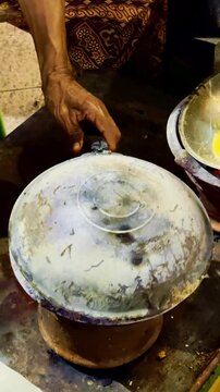 Covered metal pan cooks over a charcoal stove beside a freshly prepared golden omelet.