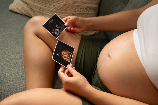 Pregnant woman on couch holding sonogram images