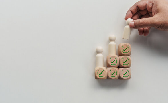 Hand placing wooden human figure on checkmark blocks representing employee selection, recruitment process, candidate evaluation, hiring decision, quality assurance, compliance approval management