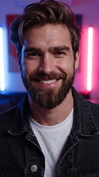 A smiling bearded man poses in a neon lit modern room