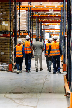 Group of workers and supervisor walking through warehouse aisles, inspecting inventory and discussing operations