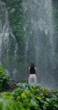 Woman standing before tropical waterfall surrounded by lush rainforest in Bali, Indonesia. Slow motion