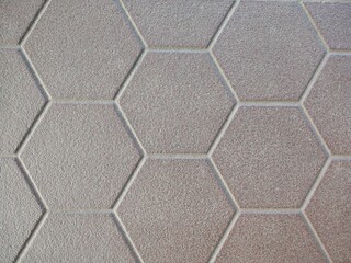 The surface is laid with hexagonal tiles in a gray-beige color with a matte, rough texture. Clear, light-colored grout creates a geometric honeycomb pattern, suitable for use as a background