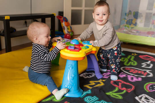 Cheerful twin brothers joyfully explore a musical activity table, learning to stand and play together in their sunny playroom