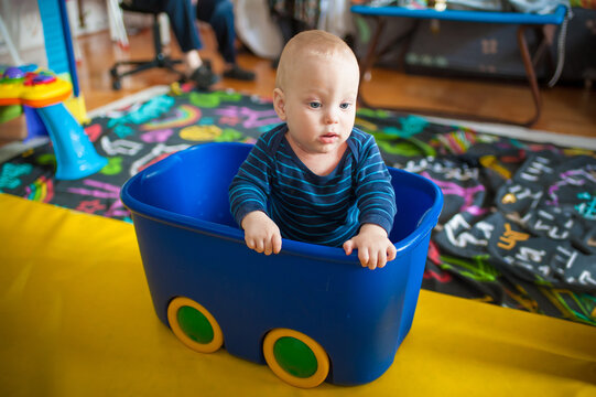 Curious baby boy sitting inside a vibrant blue plastic storage bin acting like a makeshift train car during a cheerful afternoon of indoor playtime