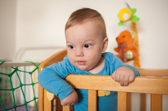 Curious toddler resting his small hands on the wooden railing of his cozy crib while observing the bright morning surroundings in his peaceful bedroom