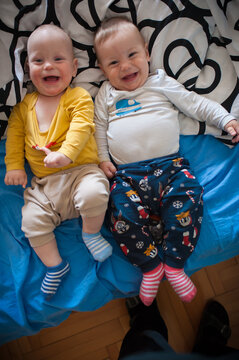 Radiant twins share contagious laughter on a sunlit bed, showcasing a beautiful bond of sibling love and innocent happiness in their warm sanctuary