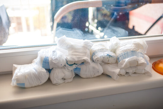 Soft white baby diapers neatly stacked upon a sunlit windowsill during a bright morning inside a cozy home nursery awaiting a playful little child
