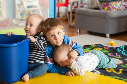 Three brothers share a tender moment of connection while playing together on a sunny afternoon in their cozy home nursery room as they explore toys