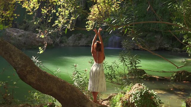 A woman balances on a fallen log above a calm forest pond