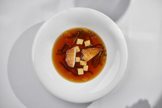 Gourmet mushroom consomme soup with grilled king oyster mushrooms, croutons, and a glass of mint water on a sunny restaurant table.
