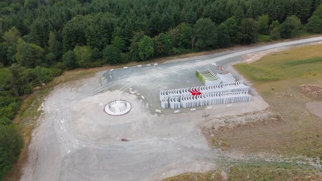 Construction site, preparation for building wind turbine farm, concrete tower section, foundation area, rows of curved segments, gravel ground in forest, Germany