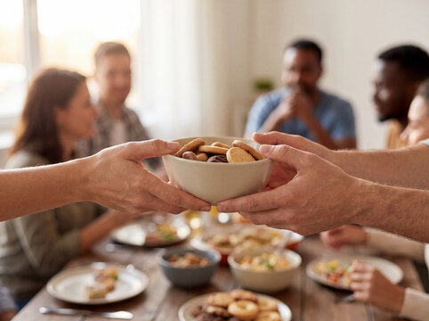 Hands passing a white bowl of cookies across a long table with plates of food at a diwali potluck