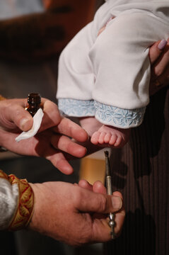 Close-up of a priest's hands anointing a baby's foot with holy oil during a traditional Orthodox baptism or christening ceremony in a church.