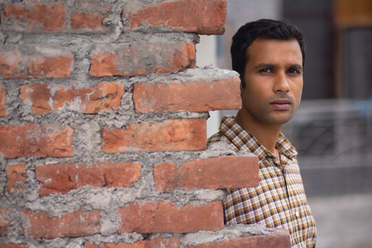 Portrait of young man standing behind brick wall