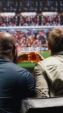 Vertical video: Football supporters watch live match broadcast at home creating realistic stadium feeling while soccer fans enjoy immersive stadium viewing.