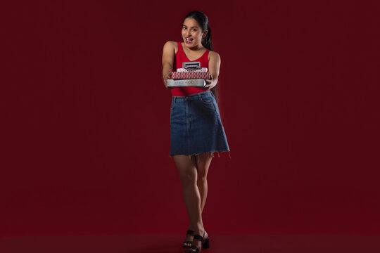 Teenage girl standing with gift boxes against maroon background