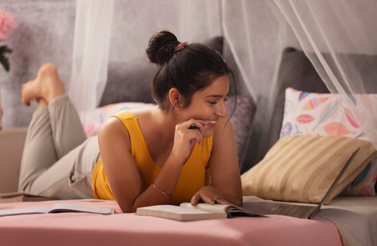 Teenage girl lying on bed and studying with laptop
