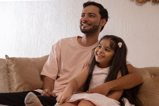 Father and daughter looking away while sitting together on sofa at home