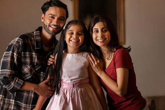 Portrait of happy couple with their girl child looking at camera at home