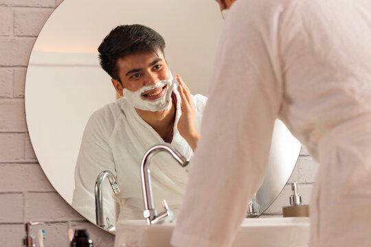 Young man applying shaving cream to his face in a bathroom at home