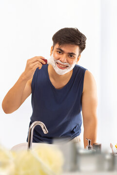 Young man applying shaving cream to his face in  bathroom at home