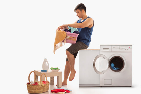 Young man sitting near washing machine with laundry basket