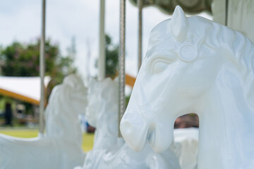 White Carousel Horses in Focus: The detailed marble heads of white carousel horses stand out in sharp focus, with blurred background suggesting an outdoor amusement park setting. © bubbers