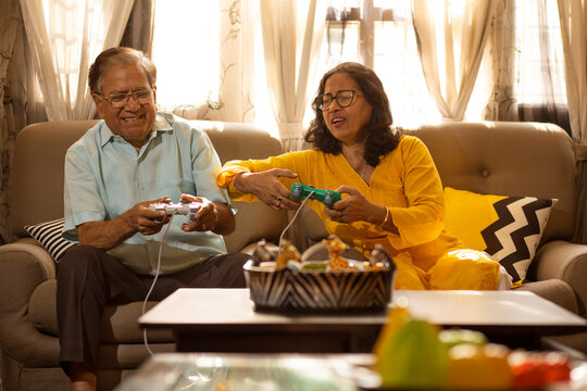 Mature couple playing video game sitting together on sofa in living room
