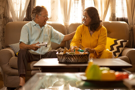 Mature couple playing video game sitting together on sofa in living room