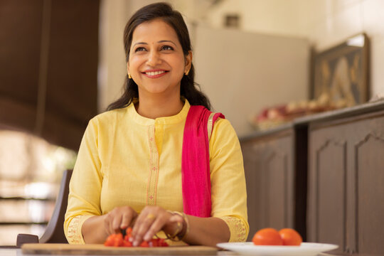 Smiling young woman chopping vegetable at home