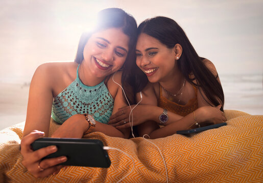Two female friends listening to music while lying down on beach