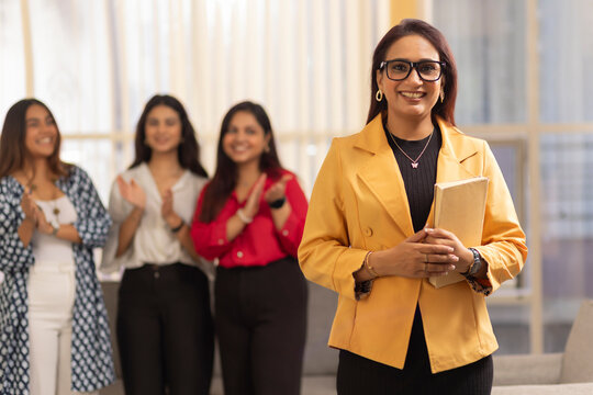 Portrait of a young businesswoman standing with notebook in an office with her colleagues in the background