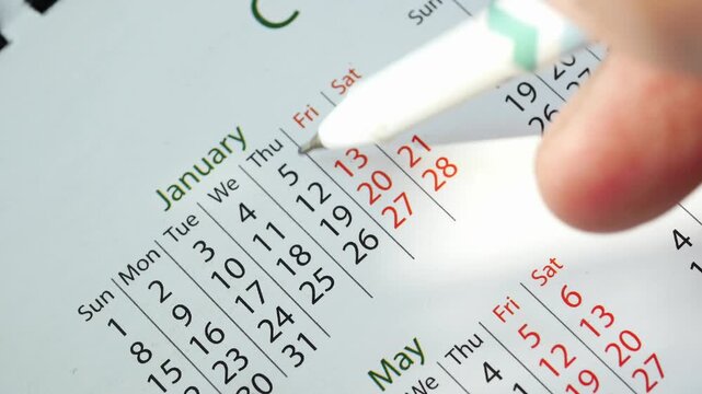 Close up view of hand circling dates on january calendar with black marker