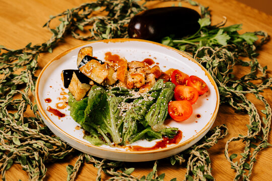 Roasted eggplant slices served with fresh green salad and cherry tomatoes on a white ceramic plate