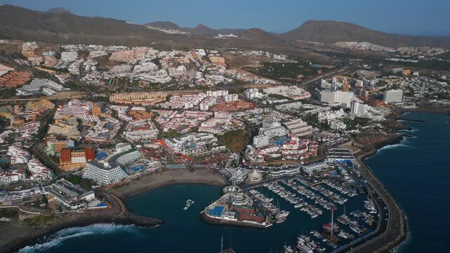 Aerial drone view of Costa Adeje marina coastline and resort hotels in Tenerife Spain, Panoramic Atlantic waterfront with yachts beaches mountains and popular holiday destination 4k
