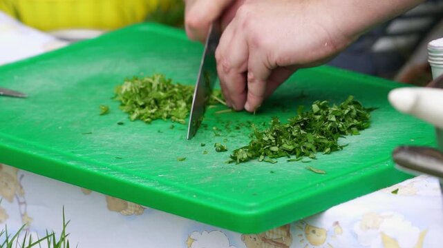 Close-up shot of hands skillfully chopping fresh green herbs on a vibrant cutting board outdoors, featuring natural lighting and sharp focus.