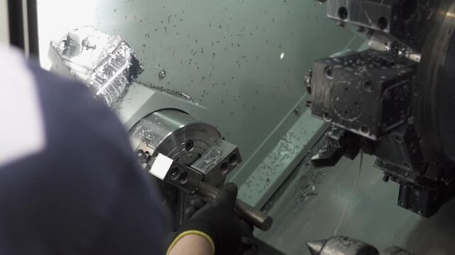 Operator installs metal rod in a CNC lathe, adjusting controls in a well-lit industrial setting. Modern machining, precision engineering in action.