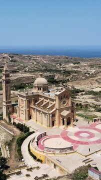 Vertical aerial footage of Ta' Pinu National Shrine in Gharb, Malta, showcasing detailed architecture, scenic countryside, and vibrant blue skies. Ideal for social media.