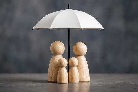 Family Life Insurance Protection. Wooden peg dolls representing a family standing under a protective umbrella.