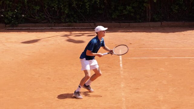 Male tennis player preparing low backhand return on outdoor clay court. Concept of tennis training, quick reactions, competitive performance, athletic skills, precision and active lifestyle.