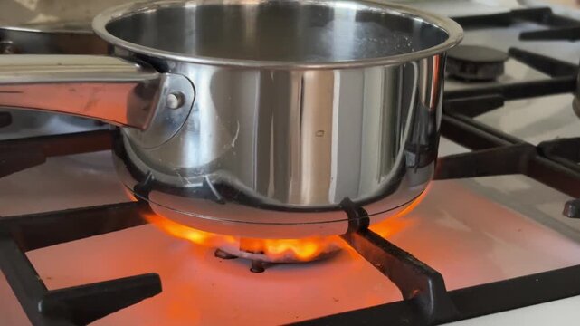 Bright orange flame burning on a gas stove burner under a metal saucepan, home cooking and domestic energy concept