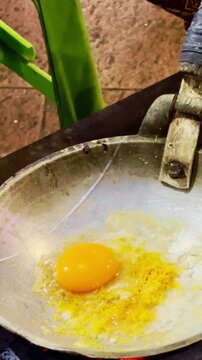 Fresh egg mixture cooks in a metal pan over charcoal during traditional Indonesian street food preparation.