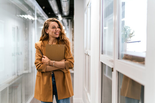 Smiling businesswoman with note pad standing near window at office