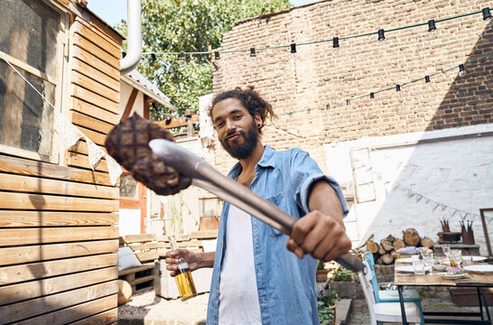 Young man preparing meat on a barbecue grill in a backyard