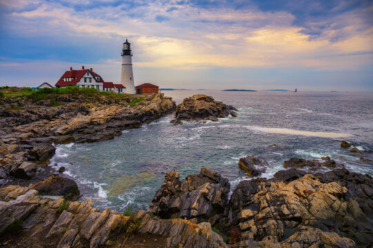 Sunset view of Portland Head Lighthouse overlooking rocky shoreline and calm ocean waters in Cape Elizabeth, Maine, USA.